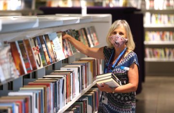 Female librarian wearing a mask, stacking books on to a library shelf
